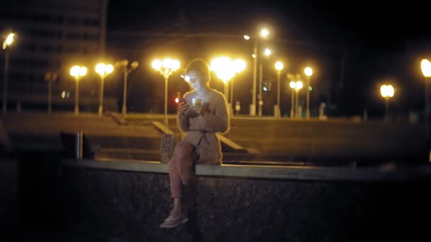 Jovem mensagem de texto mulher no telefone celular, enquanto o centro da cidade à noite. mensagens de texto feminino feliz com smartphone na cidade . — Vídeo de Stock