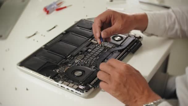 Um homem está a reparar um portátil. O conceito de reparação de computadores. Fechar-se de homem reparar placa-mãe laptop com uma chave de fenda. Manutenção do hardware da placa-mãe. Suporte de disco, reparação de computadores — Vídeo de Stock