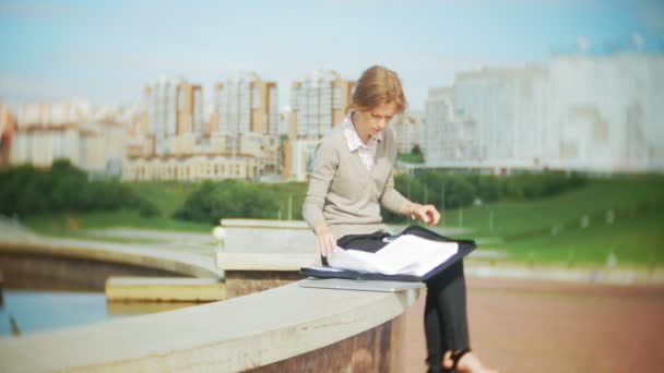 Young business woman sitting on the steps with a laptop in the business center, reading documents. — Stock Video