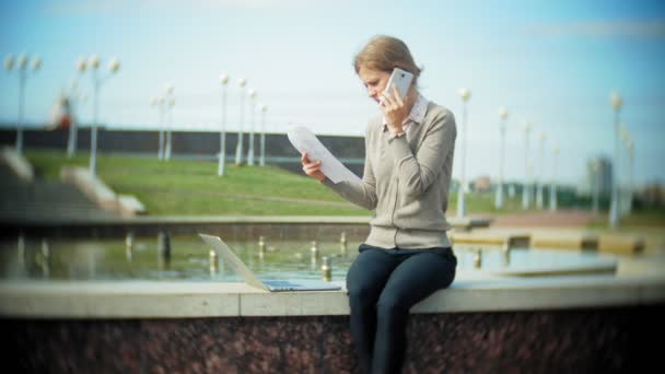 Young business woman sitting on the steps with a laptop in the business center, reading documents. — Stock Video