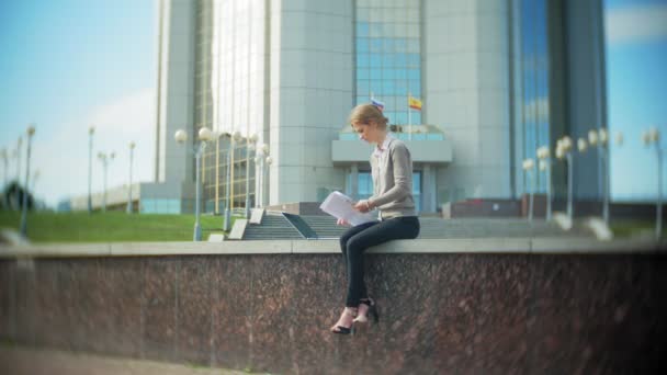 Jeune femme d'affaires assise sur les marches avec un ordinateur portable dans le centre d'affaires, lire des documents . — Video