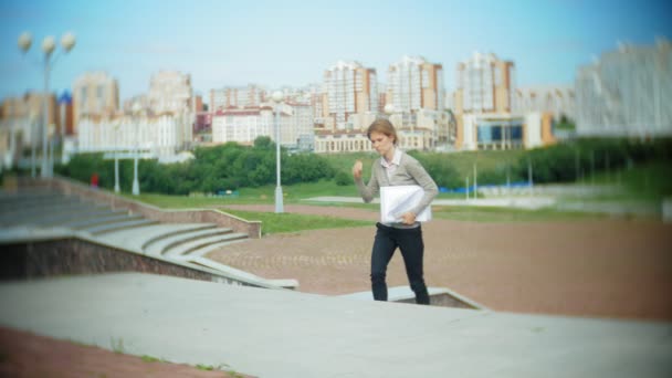 Young business woman sitting on the steps with a laptop in the business center, reading documents. — Stock Video