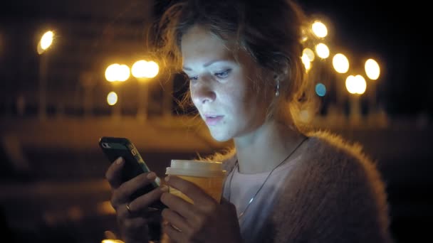 Mensajería de texto de mujer joven en el teléfono móvil mientras está en el centro por la noche. Mensajes femeninos felices con smartphone en la ciudad . — Vídeos de Stock