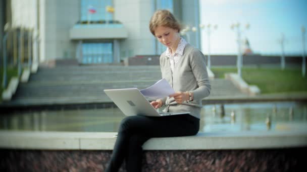 Jonge zakelijke vrouw zitten op de trappen met een laptop in het business center, documenten te lezen. — Stockvideo