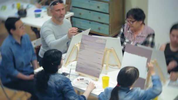 École d'art, concept de créativité et de personnes - groupe d'étudiants avec des chevalets, pinceaux et palettes peinture nature morte à l'atelier, les personnes âgées et les jeunes dessinent — Video