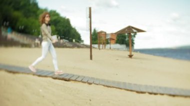 Genç güzel kadın kulaklık Beach'te yürüyor ve bir tablet kullanır