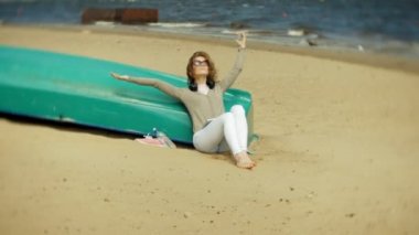 Genç güzel kadın kulaklık tekne yakınındaki kumsalda oturur ve bir tablet kullanır
