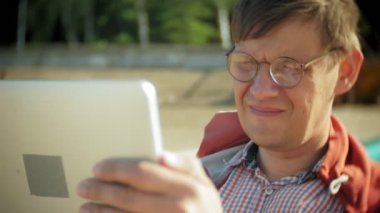 Yaşlı adam kulaklık tekne yakınındaki kumsalda oturur ve bir tablet kullanır