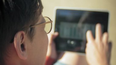 Yaşlı adam kulaklık tekne yakınındaki kumsalda oturur ve bir tablet kullanır