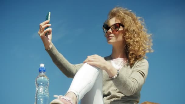 Egy nő használ egy okostelefon a tengerparton — Stock videók
