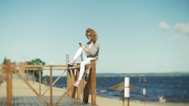 Una mujer utiliza un teléfono inteligente en la playa de — Vídeo de stock