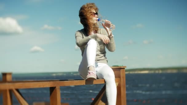 Mujer bebiendo agua de una botella en la playa — Vídeo de stock