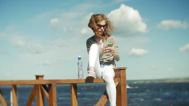 Mujer disfruta de un smartphone escuchando música en auriculares en la playa — Vídeo de stock