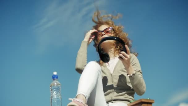 Женщина наслаждается смартфоном, слушая музыку на наушниках на пляже — стоковое видео