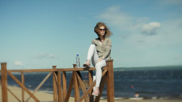 Жінка п'є воду з пляшки на пляжі — стокове відео
