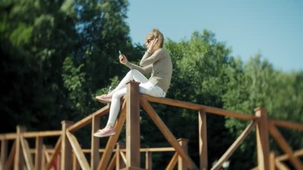 Kvinnan har en smartphone som lyssnar på musik i hörlurar på stranden — Stockvideo