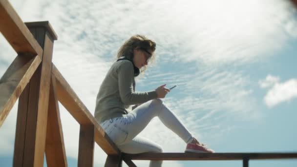 Ung vacker kvinna sitter på stranden i hörlurar och använder en surfplatta — Stockvideo