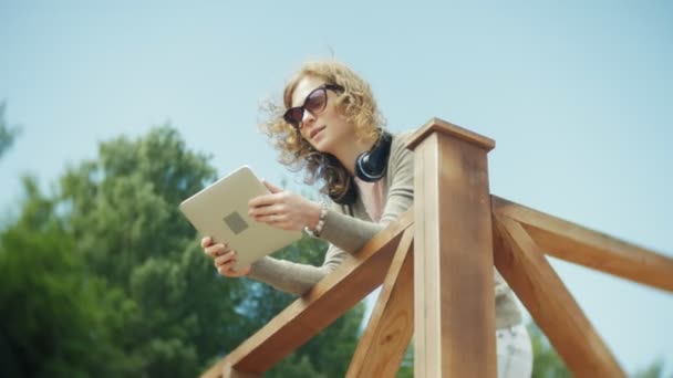 Mladá krásná žena se nachází na pláži v sluchátka a používá tablet — Stock video