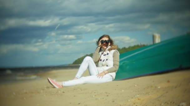 Jeune femme assise sur la plage à l'extérieur du bateau et regarde à travers les jumelles — Video