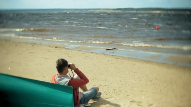 Äldre Man Sitter Stranden Utanför Båten Och Ser Genom Kikare — Stockvideo