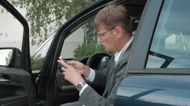Зрелый бизнесмен в машине пользуется смартфоном — стоковое видео
