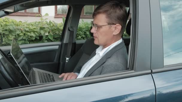 Зрелый бизнесмен в машине работает на ноутбуке — стоковое видео