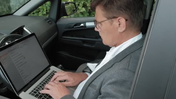 Зрілий бізнесмен в машині працює на ноутбуці — стокове відео
