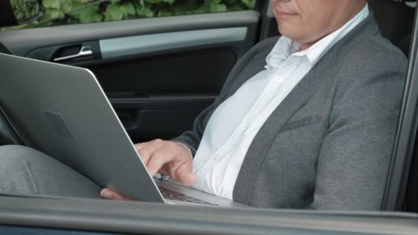 Rijpe zakenman in auto die op laptop werkt — Stockvideo