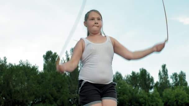 Маленька товста дівчинка стрибає мотузкою на стадіоні — стокове відео