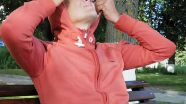 Gözlüklü bir adam parkta bir bankta oturur ve bir telefon kullanır