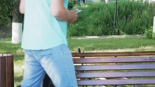 Um homem de óculos senta-se em um banco no parque e usa um telefone — Vídeo de Stock
