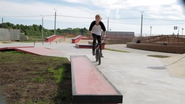 Un niño está montando trucos de ciclismo BMX en un parque de skate en un día soleado. Super cámara lenta — Vídeos de Stock