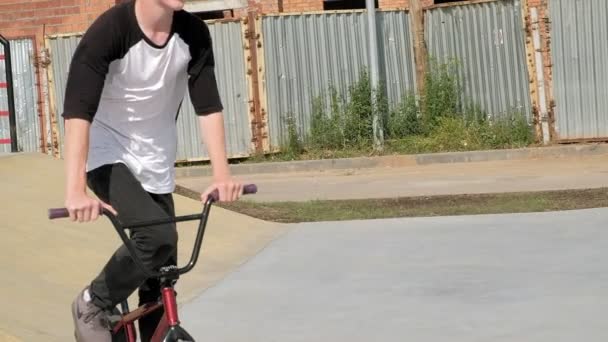 Un niño está montando trucos de ciclismo BMX en un parque de skate en un día soleado. Super cámara lenta — Vídeos de Stock