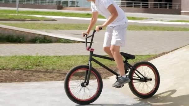 Un niño está montando trucos de ciclismo BMX en un parque de skate en un día soleado. Super cámara lenta — Vídeo de stock