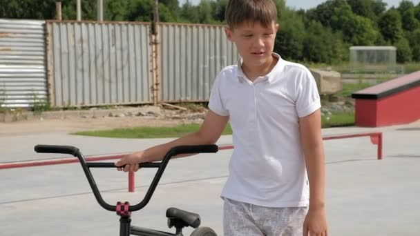 Un niño está montando trucos de ciclismo BMX en un parque de skate en un día soleado. Super cámara lenta — Vídeo de stock