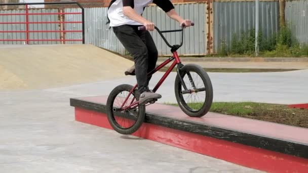 Un niño está montando trucos de ciclismo BMX en un parque de skate en un día soleado. Super cámara lenta — Vídeos de Stock