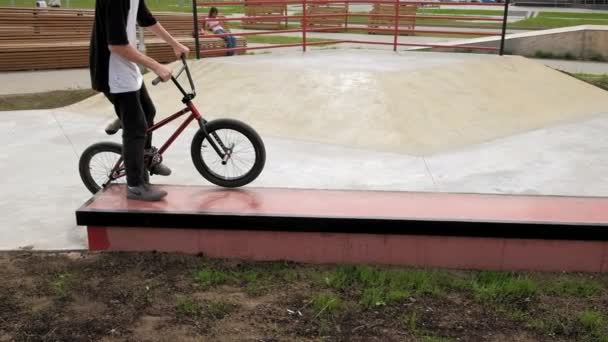 Um menino está montando BMX truques de ciclismo em um parque de skate em um dia ensolarado. Movimento super lento — Vídeo de Stock