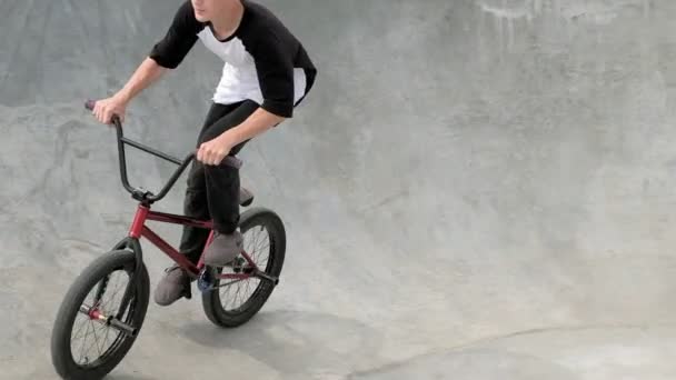 Un niño está montando trucos de ciclismo BMX en un parque de skate en un día soleado. Super cámara lenta — Vídeos de Stock