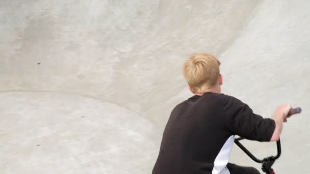 Un niño está montando trucos de ciclismo BMX en un parque de skate en un día soleado. Super cámara lenta — Vídeos de Stock