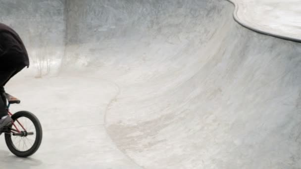 Un niño está montando trucos de ciclismo BMX en un parque de skate en un día soleado. Super cámara lenta — Vídeos de Stock