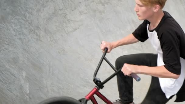 Un niño está montando trucos de ciclismo BMX en un parque de skate en un día soleado. Super cámara lenta — Vídeos de Stock