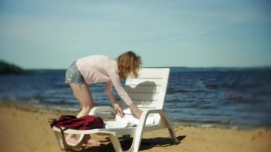 Genç kız yatıyor ve deniz kumlu plajda şezlong üzerinde sunbathes