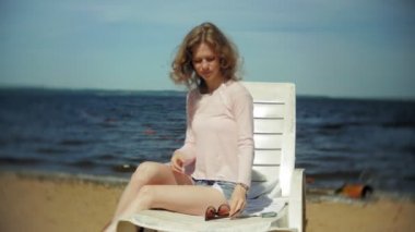 Genç kız yatıyor ve deniz kumlu plajda şezlong üzerinde sunbathes