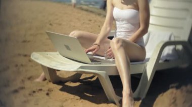 Beyaz bikinili genç bir kız yatıyor ve tans üzerinde bir deniz kumlu plajda şezlong ve bir dizüstü bilgisayar üzerinde çalışan