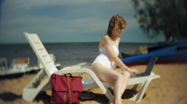 Beyaz bikinili genç bir kız yatıyor ve tans üzerinde bir deniz kumlu plajda şezlong ve bir dizüstü bilgisayar üzerinde çalışan