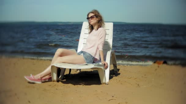 Genç kız yatıyor ve deniz kumlu plajda şezlong üzerinde sunbathes — Stok video