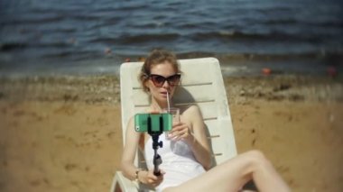 Beyaz bikinili genç bir kız yatıyor ve bir deniz kumlu plajda şezlong ve fotoğrafları Smartphone cep telefonu ile Selfi sunbathes