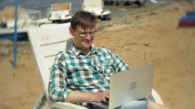 Beyaz bikinili genç bir kız yatıyor ve tans üzerinde bir deniz kumlu plajda şezlong ve bir dizüstü bilgisayar üzerinde çalışan