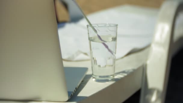 Laptop e um copo de água em uma chaise longue com vista para o oceano — Vídeo de Stock