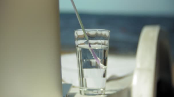 Ordinateur portable et un verre d'eau sur une chaise longue donnant sur l'océan — Video